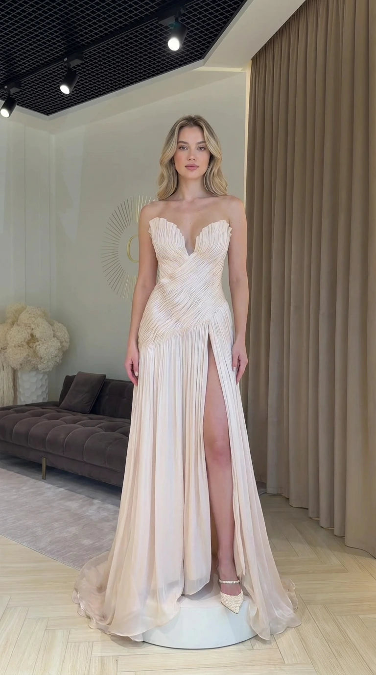 Front view of model wearing champagne strapless pleated evening dress with high slit