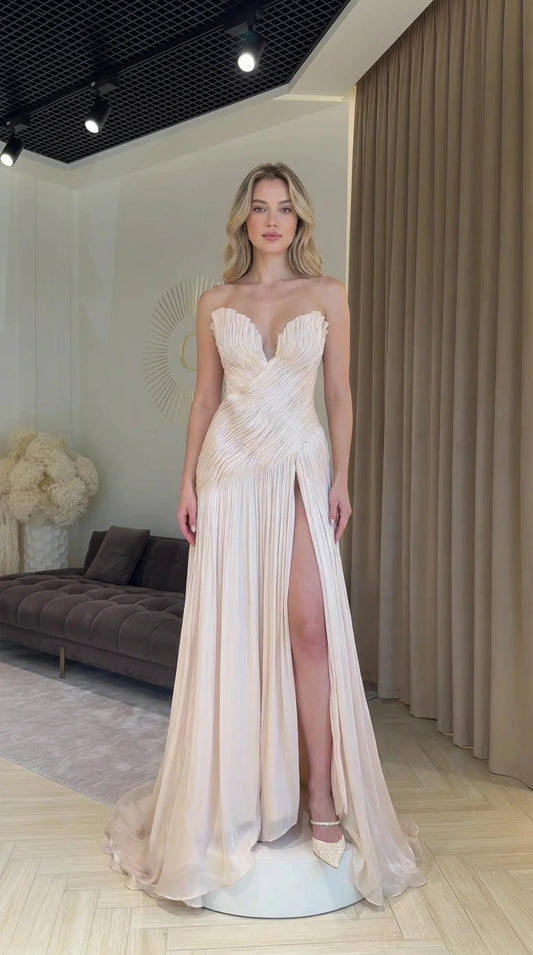 Front view of model wearing champagne strapless pleated evening dress with high slit