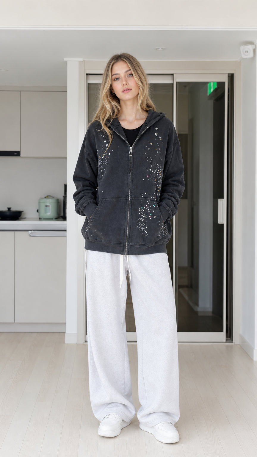 Front view of woman wearing washed black rhinestone star zip-up hoodie with white sweatpants