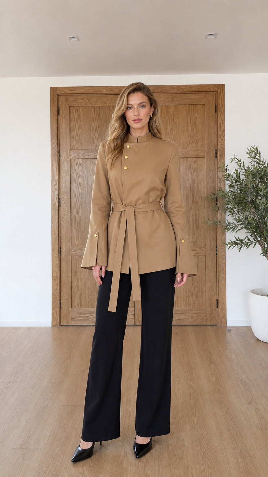 Full front view of model wearing camel asymmetrical belted tunic jacket with black trousers