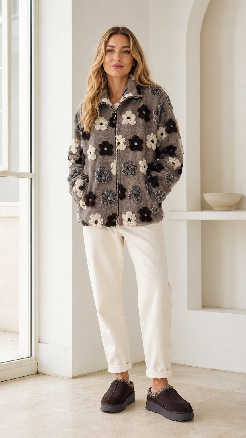 Full front view of model wearing charcoal grey floral sherpa fleece zip-up jacket with white pants