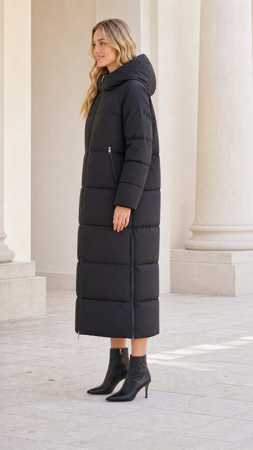 Side profile view of model wearing long black quilted puffer coat with hood up