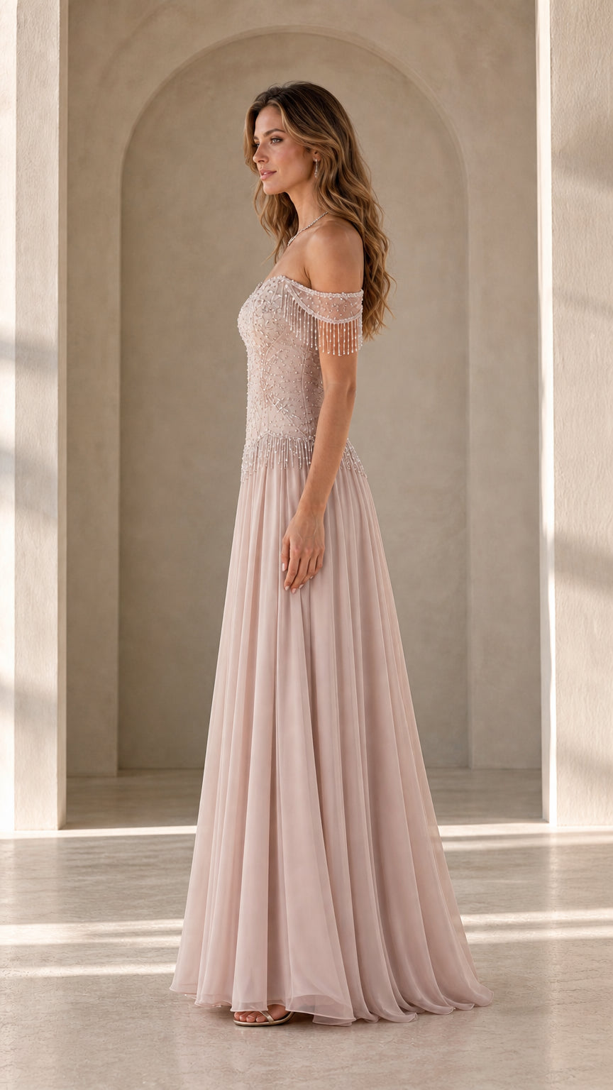 Side profile view of model in blush pink formal gown showing arm fringe detail