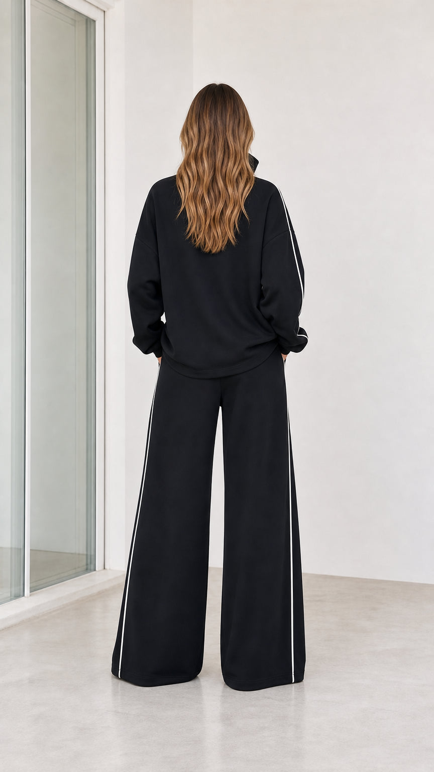 Back view of model wearing black wide leg lounge set with contrast white piping