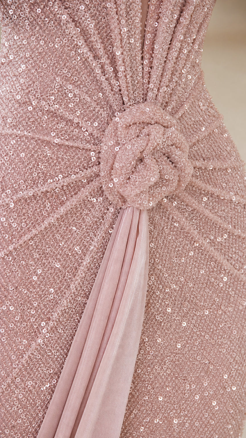 Close-up detail of blush pink sequin fabric, waist rosette knot, and draped sash