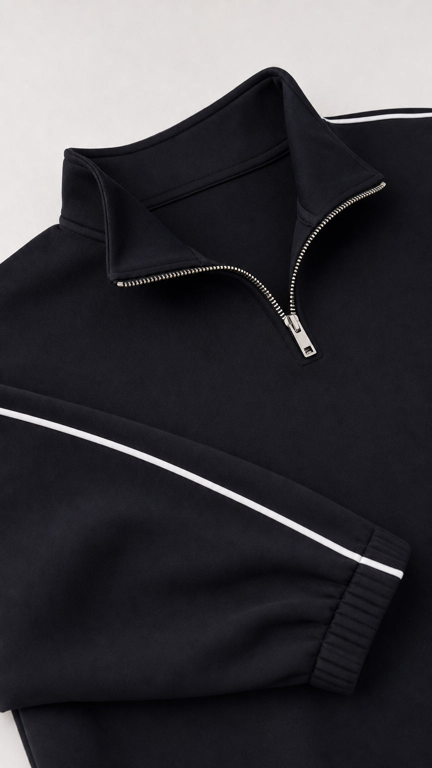 Close-up detail of black half-zip collar, metal zipper, and sleeve piping trim