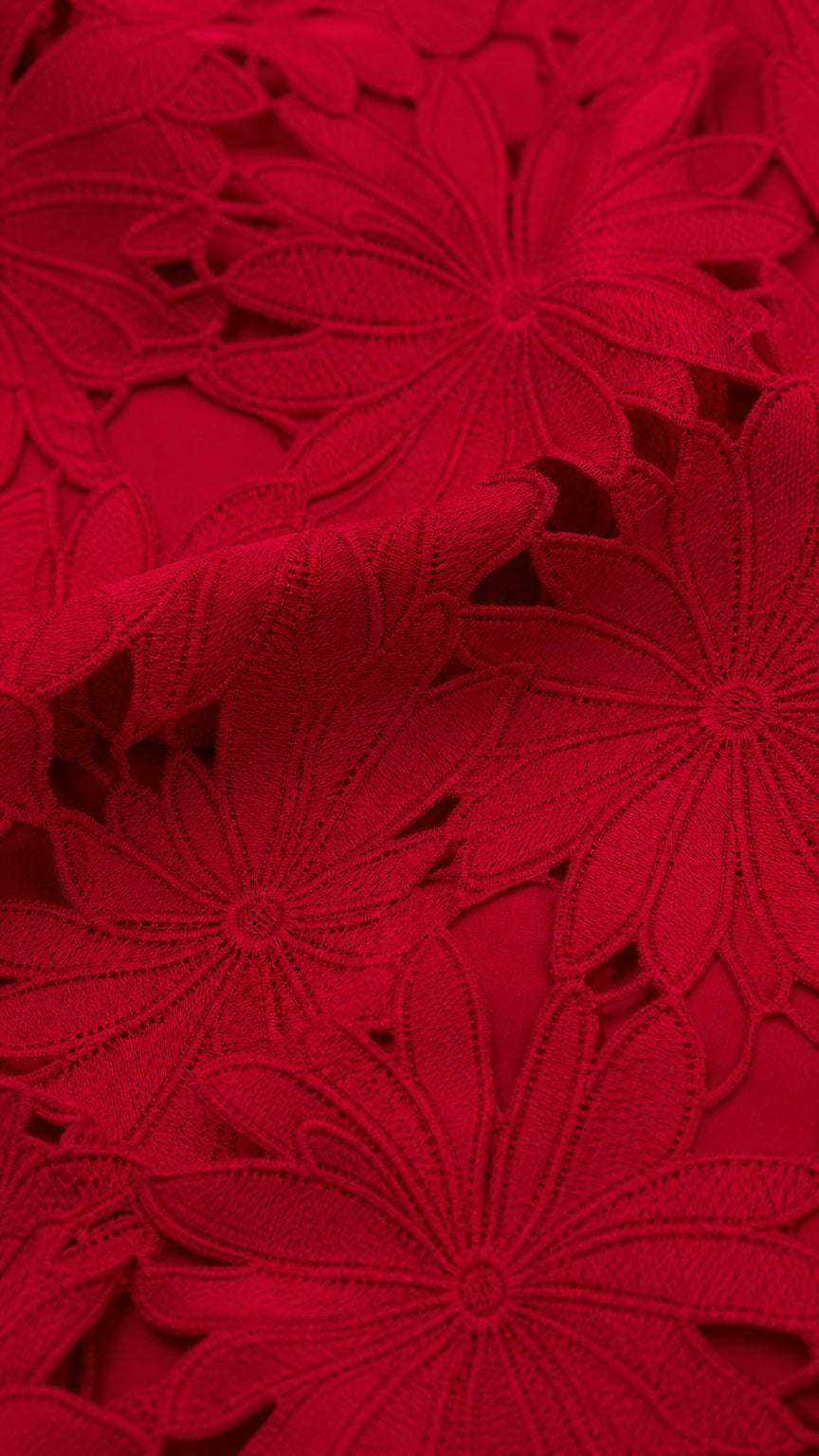Close-up detail of textured red floral lace cutout embroidery fabric