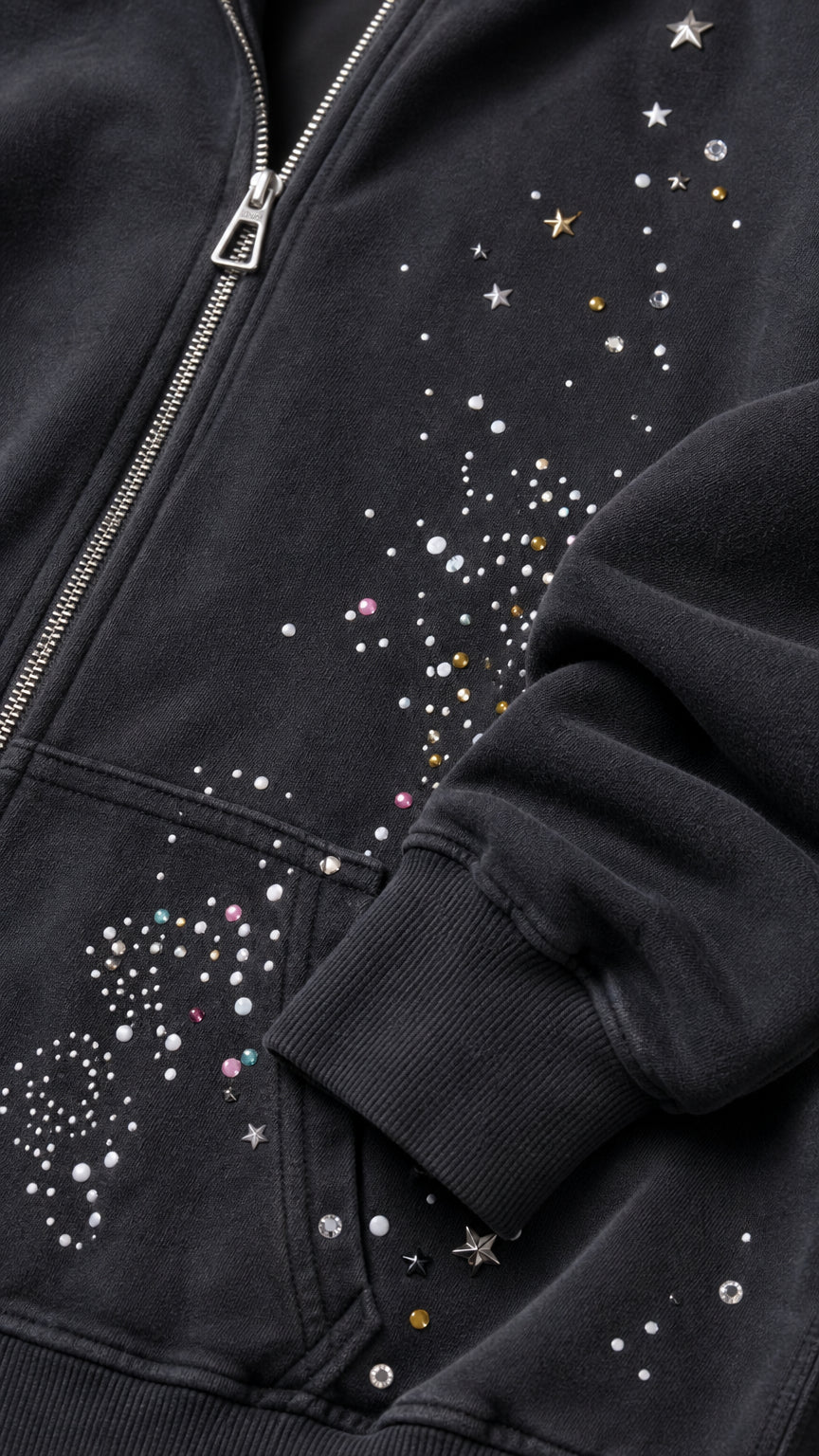 Close-up detail of rhinestone studs, star embellishments, and zipper on black hoodie pocket