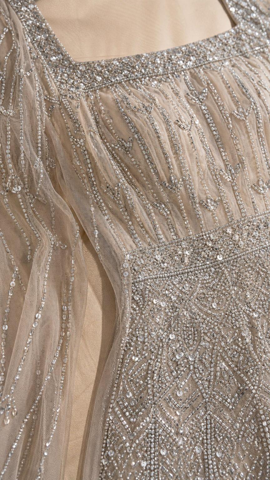 Close-up of intricate silver beadwork and square neckline on champagne mesh dress