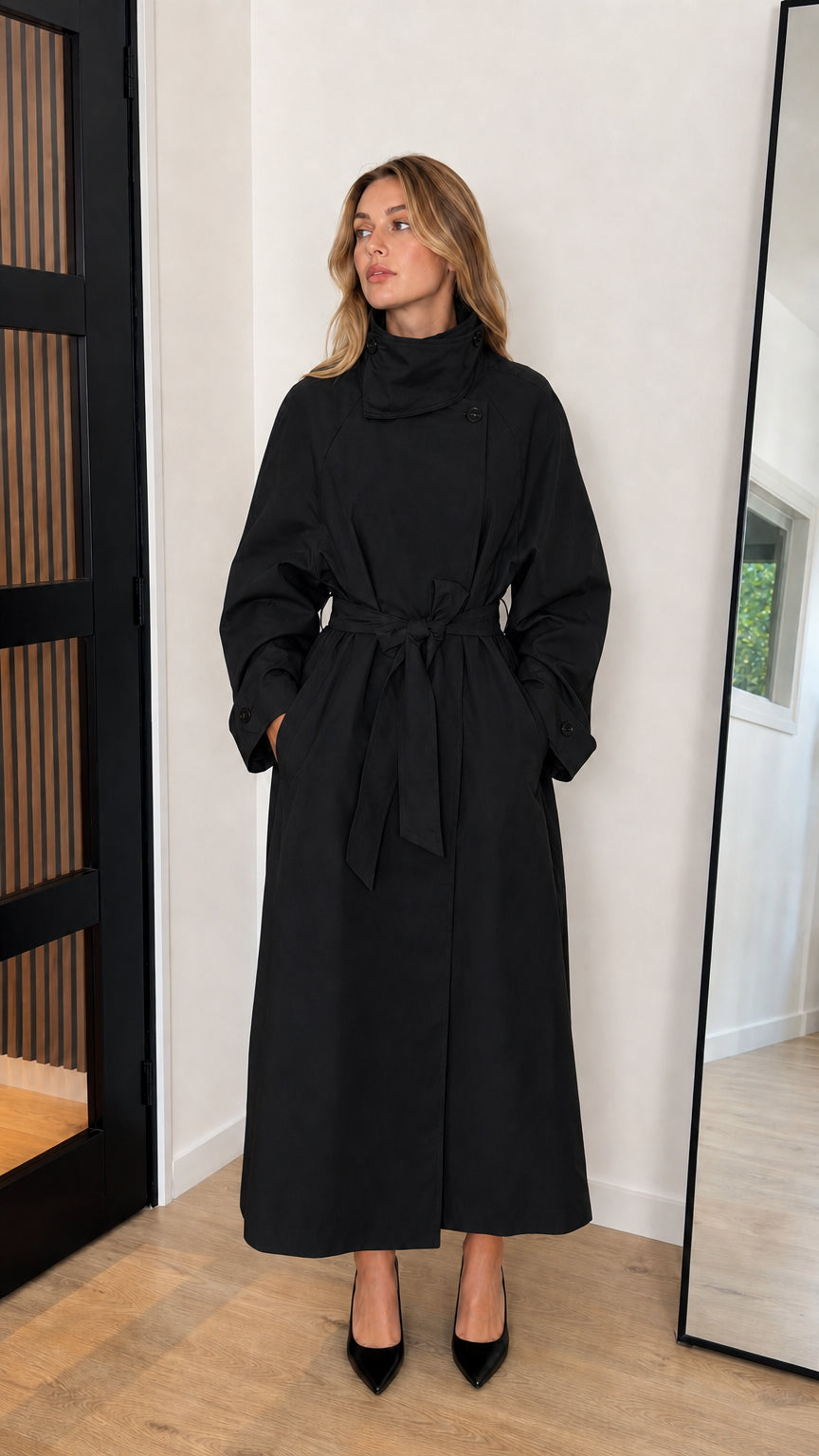 Front view of model wearing a black high neck belted longline trench coat