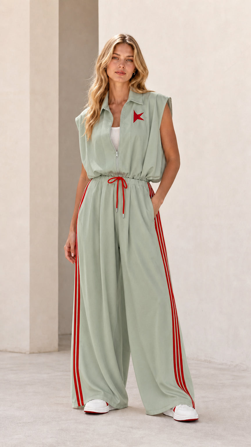 Front view of model wearing sage green sleeveless wide-leg track jumpsuit with red stripes